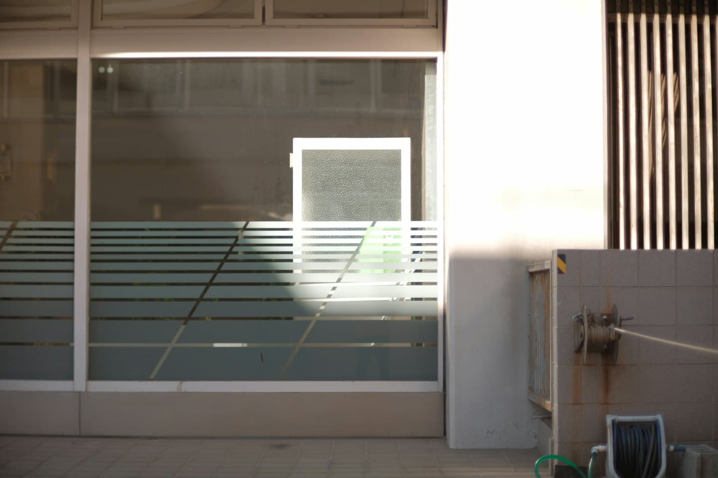 Moderne gebouw met matglazen ramen en een groene tuinslang.