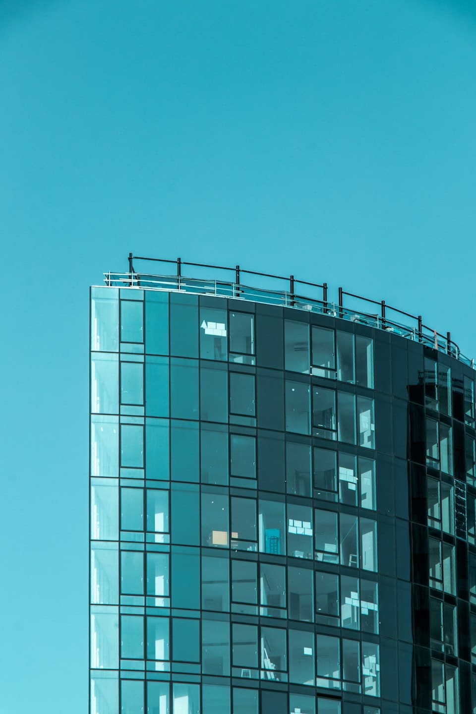 Modern glazen kantoorgebouw met gebogen gevel tegen een blauwe lucht.